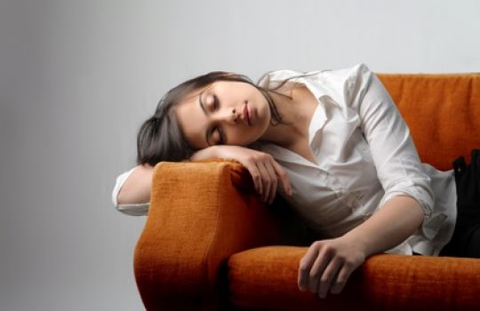 Junge Frau liegt schlafend auf dem Sofa und leidet unter Abgeschlagenheit.