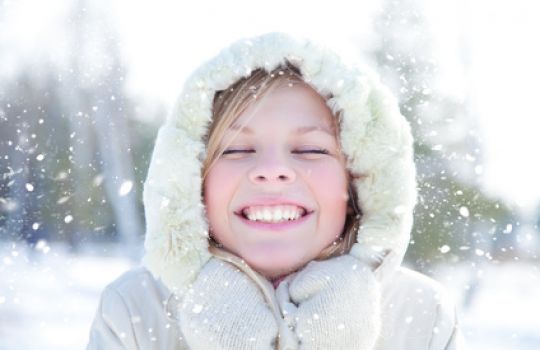 Mädchen mit Kapuze im Schnee, lächelnd.