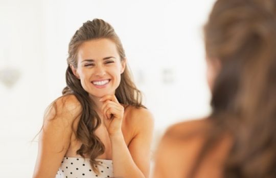 Eine Frau betrachtet sich lachend im Spiegel.