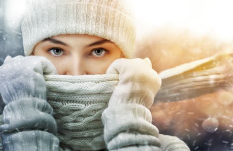 Frau schützt sich mit Schal, Handschuhen und Mütze gegen das Schneetreiben.