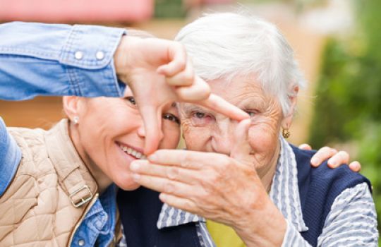 Eine junge und eine alte Frau formen ein Viereck aus ihren Händen.
